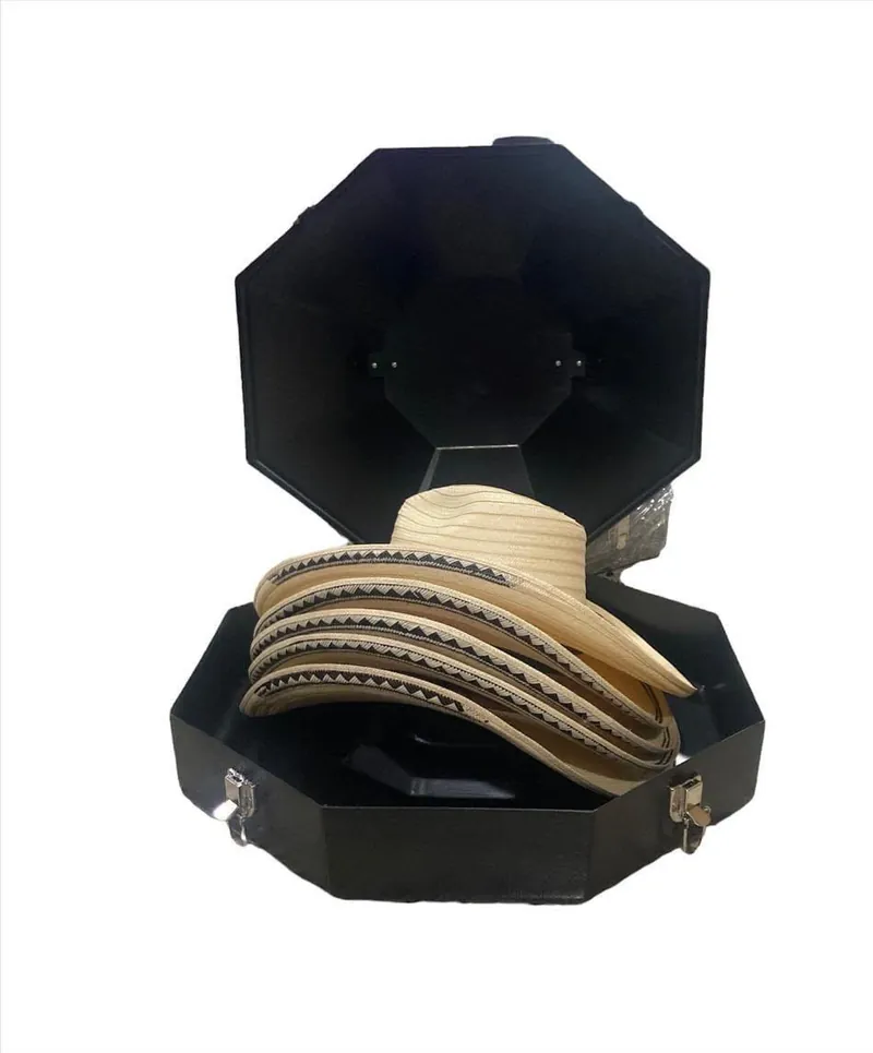 Varios sombreros claros con greca negra en zigzag al borde del ala, guardados en un estuche octogonal negro